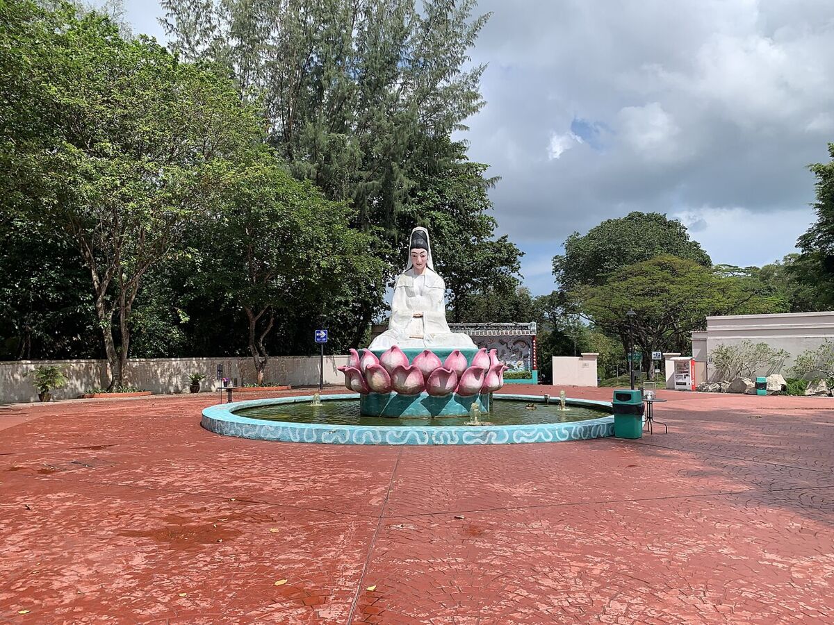 White figure seated on a pink lotus fountain in a circular pond at Haw Par Villa, Singapore