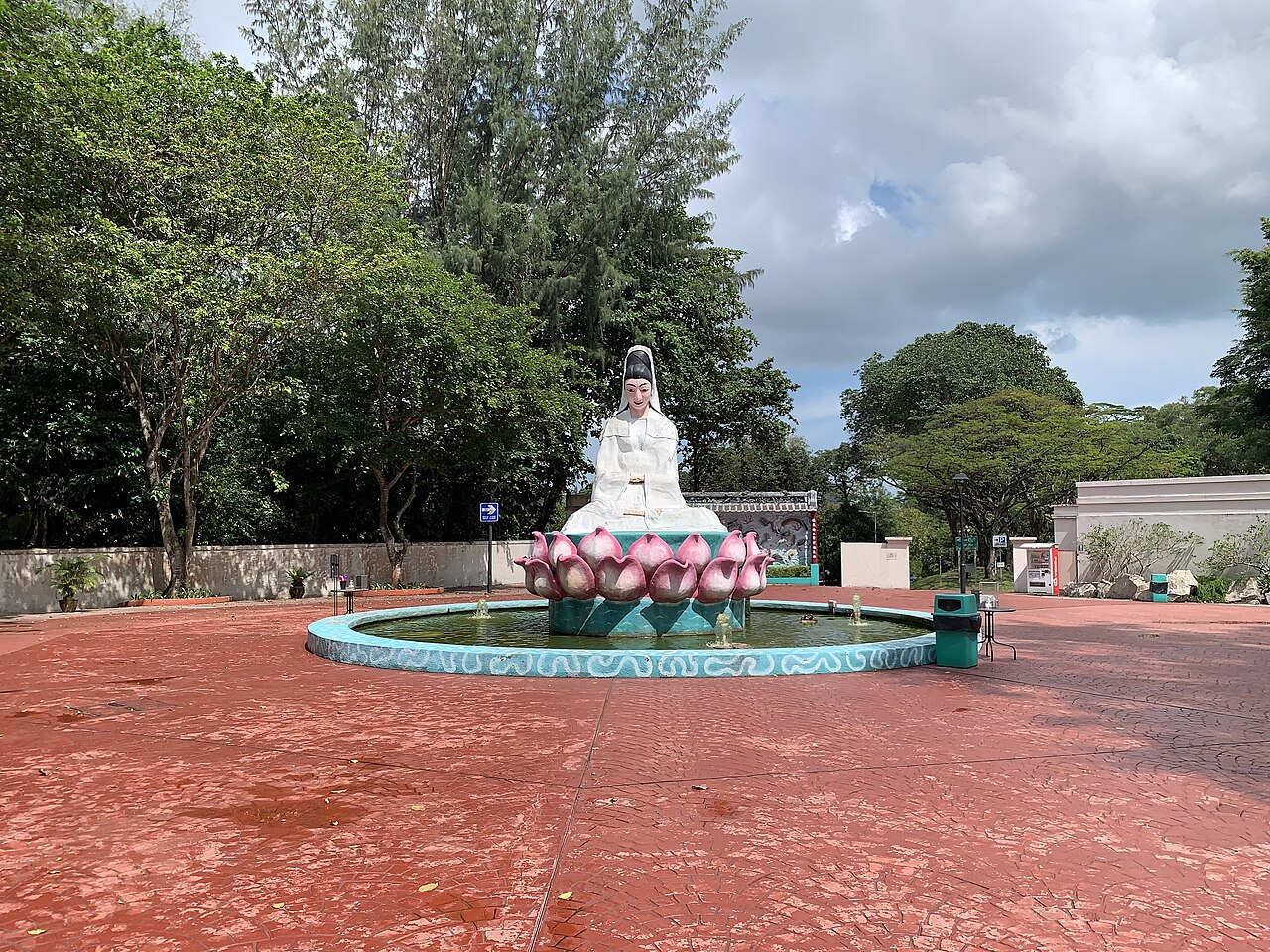White figure seated on a pink lotus fountain in a circular pond at Haw Par Villa, Singapore