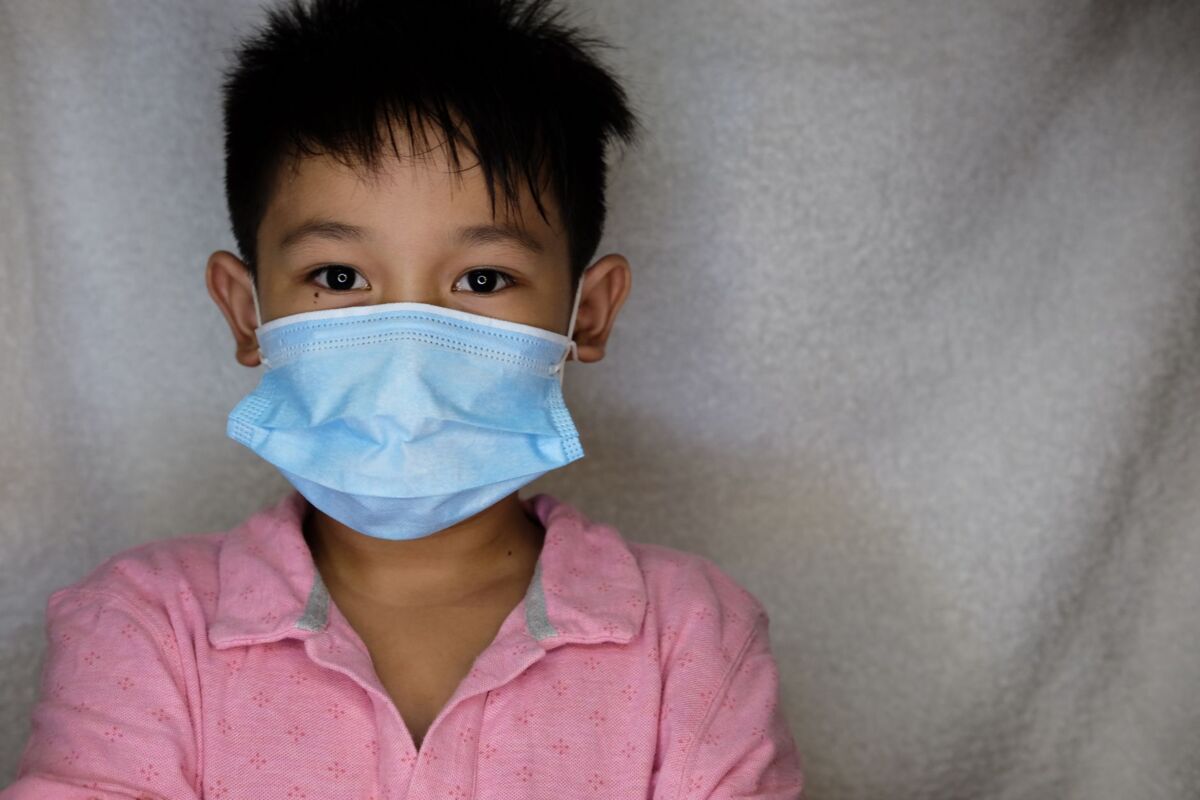 Young child wearing a blue face mask for protection during the pandemic, indoors.