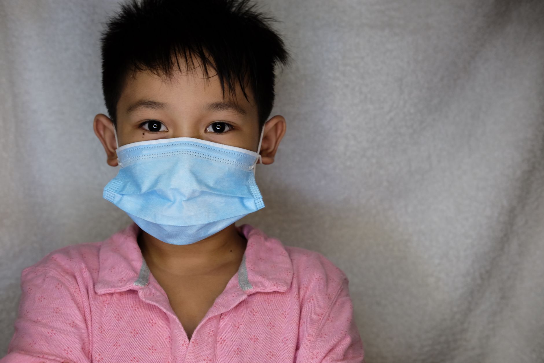 Young child wearing a blue face mask for protection during the pandemic, indoors.