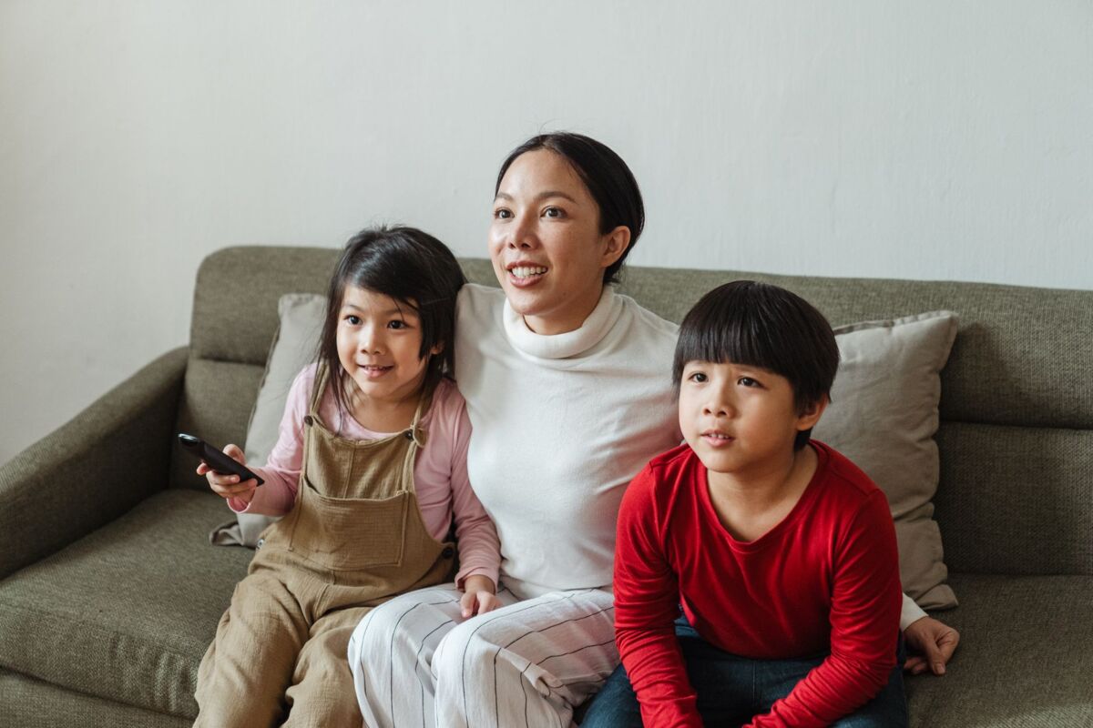 Positive Asian woman with cute kids spending weekend together at home and watching TV programs