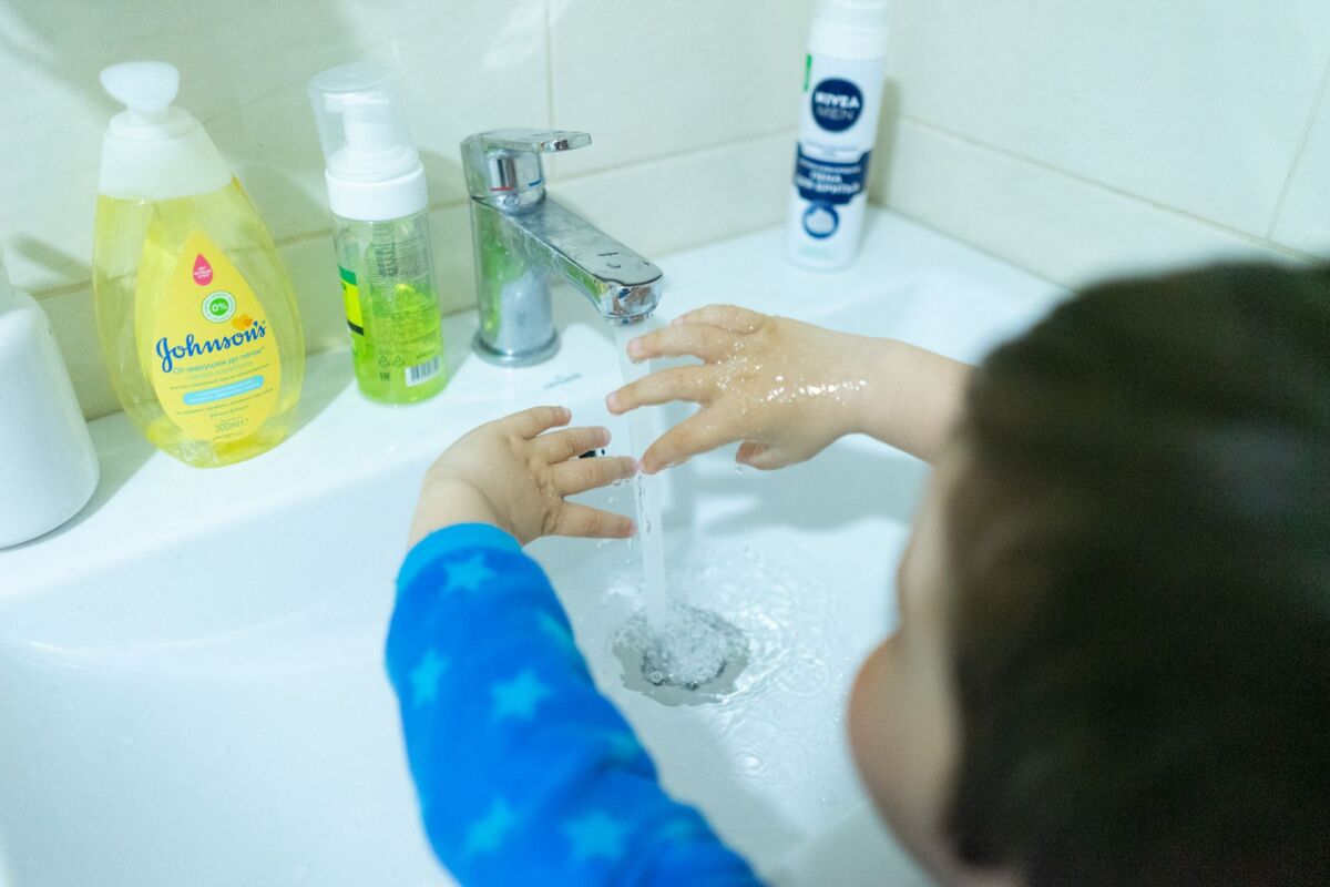 Child washing hands with soap under running water for hygiene in bathroom.
