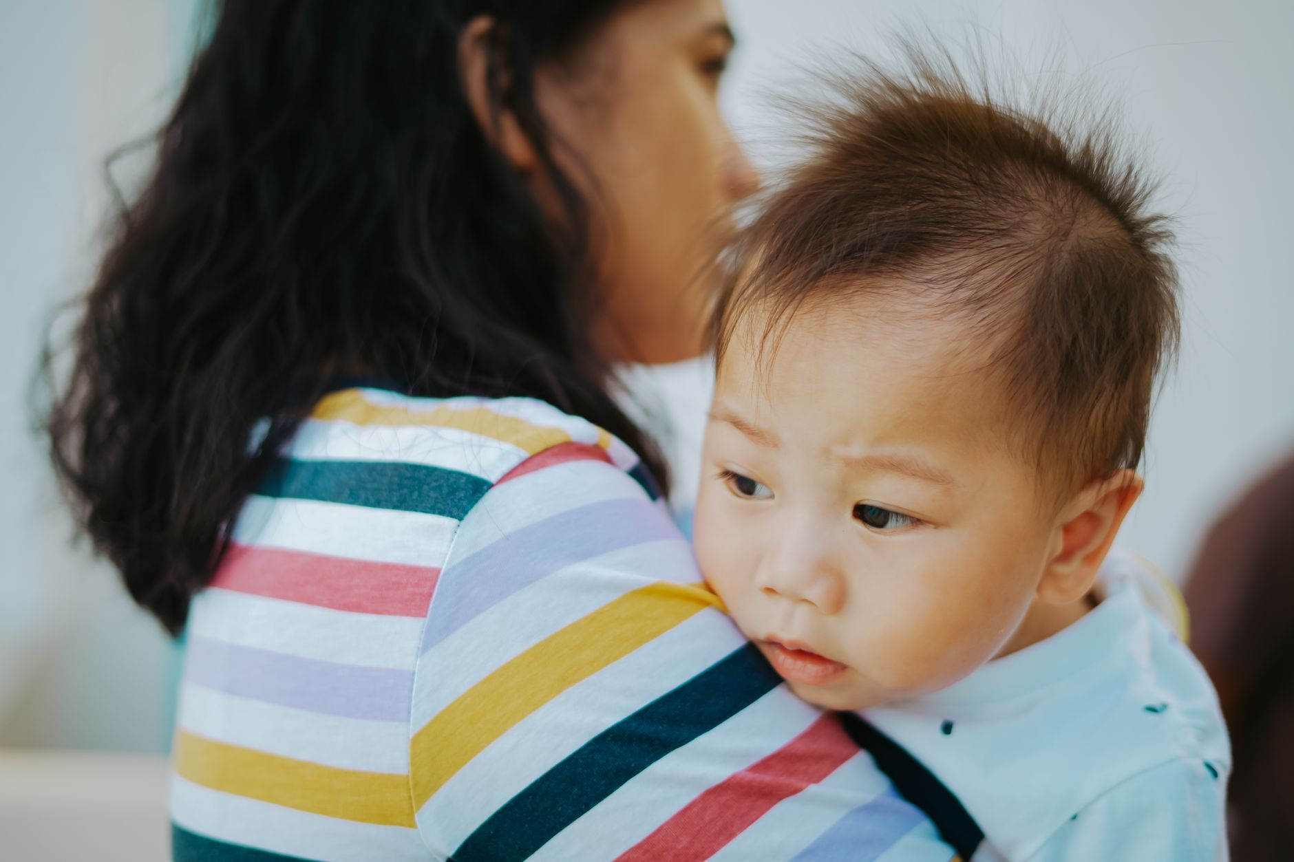 A woman lovingly holds an Asian baby boy indoors, showcasing a tender family moment.