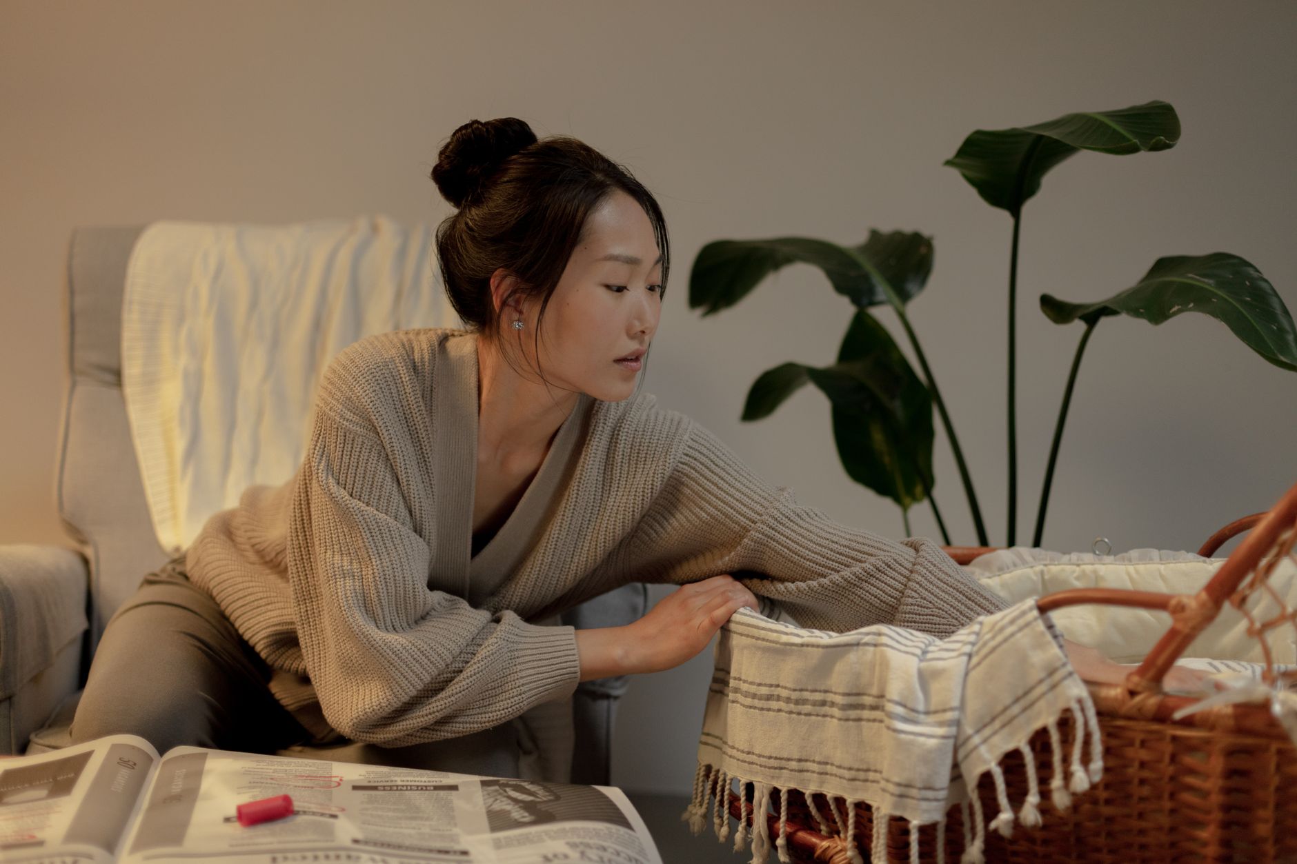 A thoughtful woman leans over a bassinet in a cozy home interior setting.