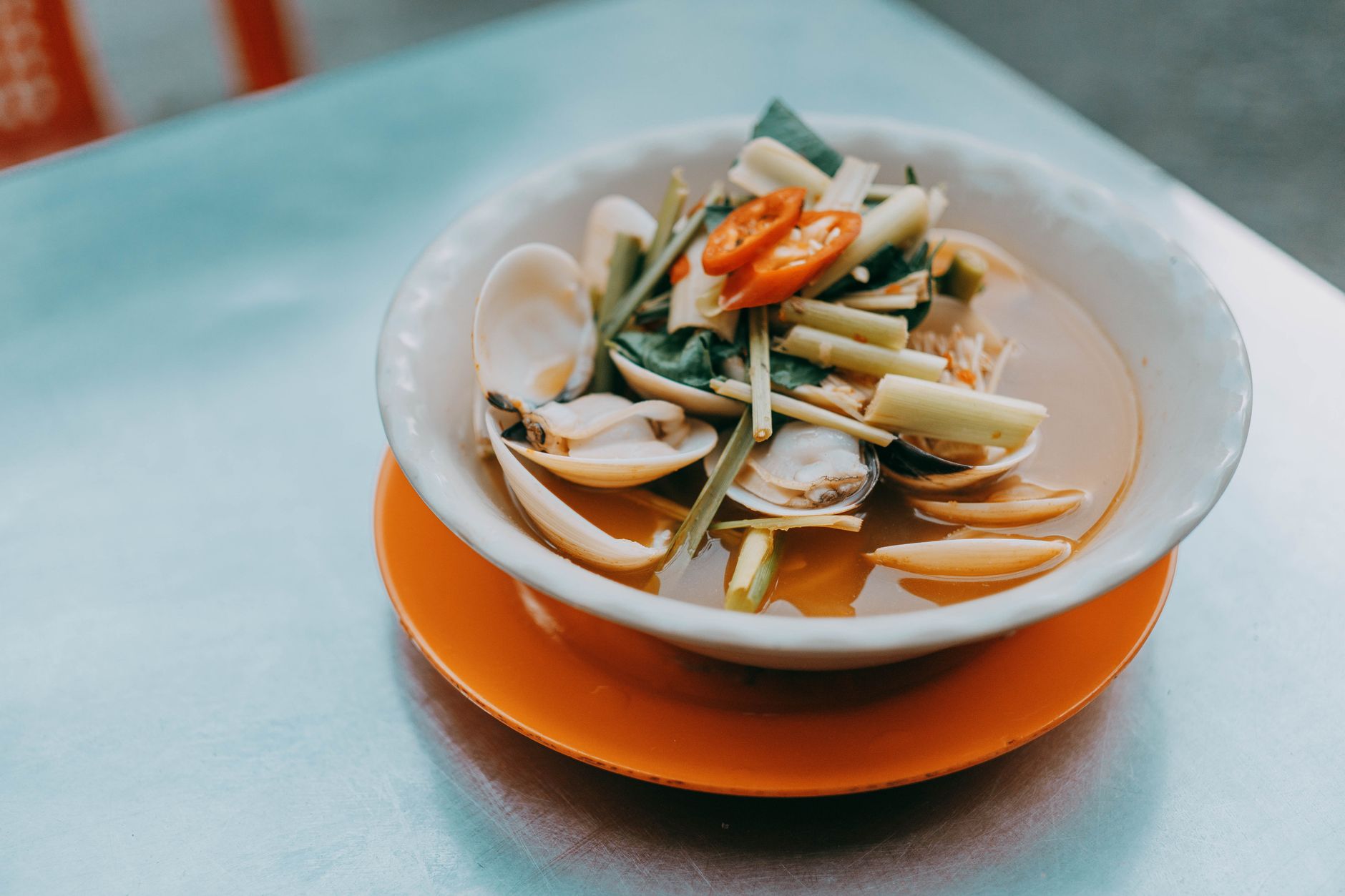 A flavorful Asian clam soup garnished with lemongrass and sliced red peppers, served in an elegant bowl.