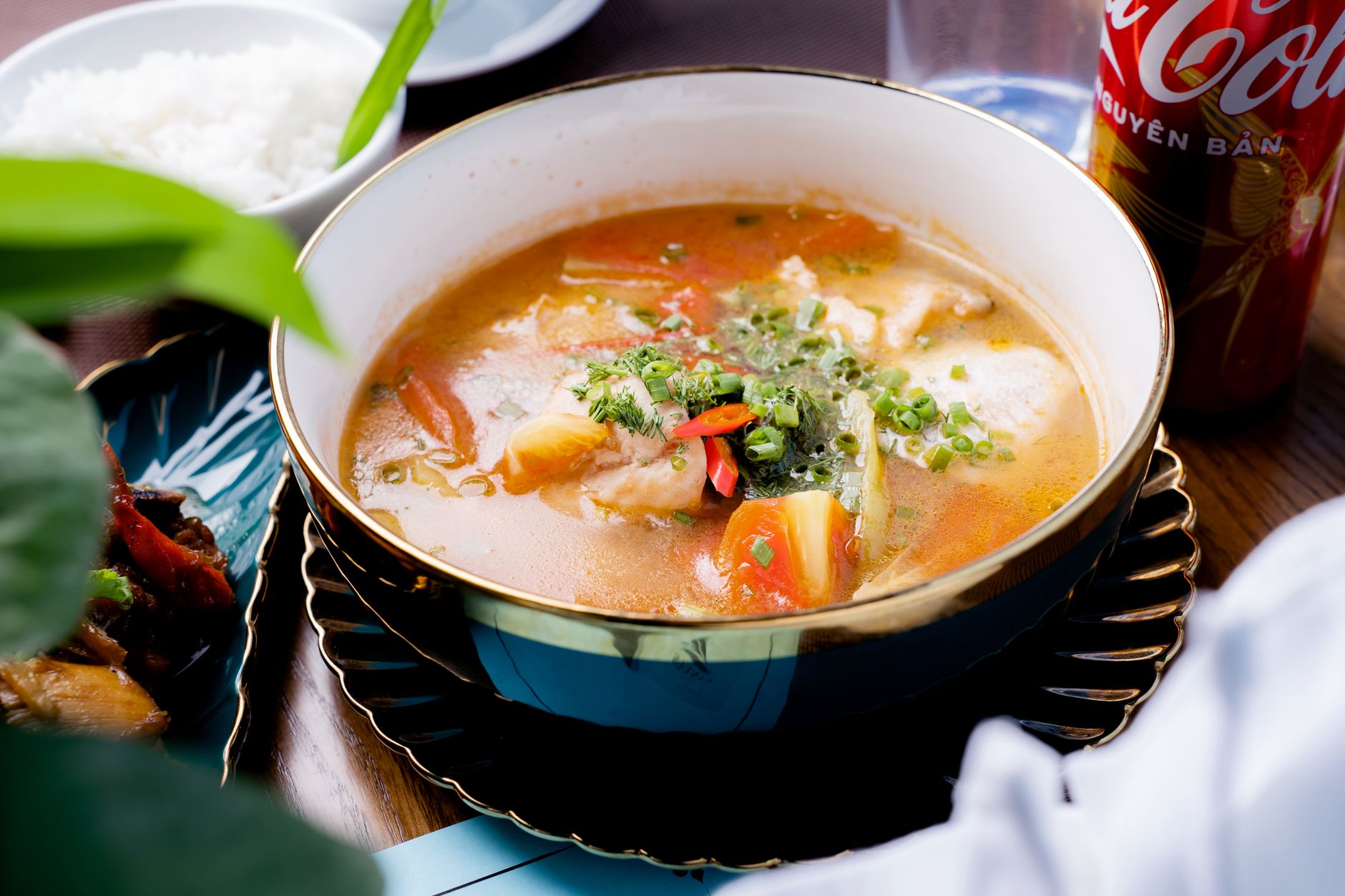A colorful bowl of Asian fish soup garnished with fresh vegetables and herbs.