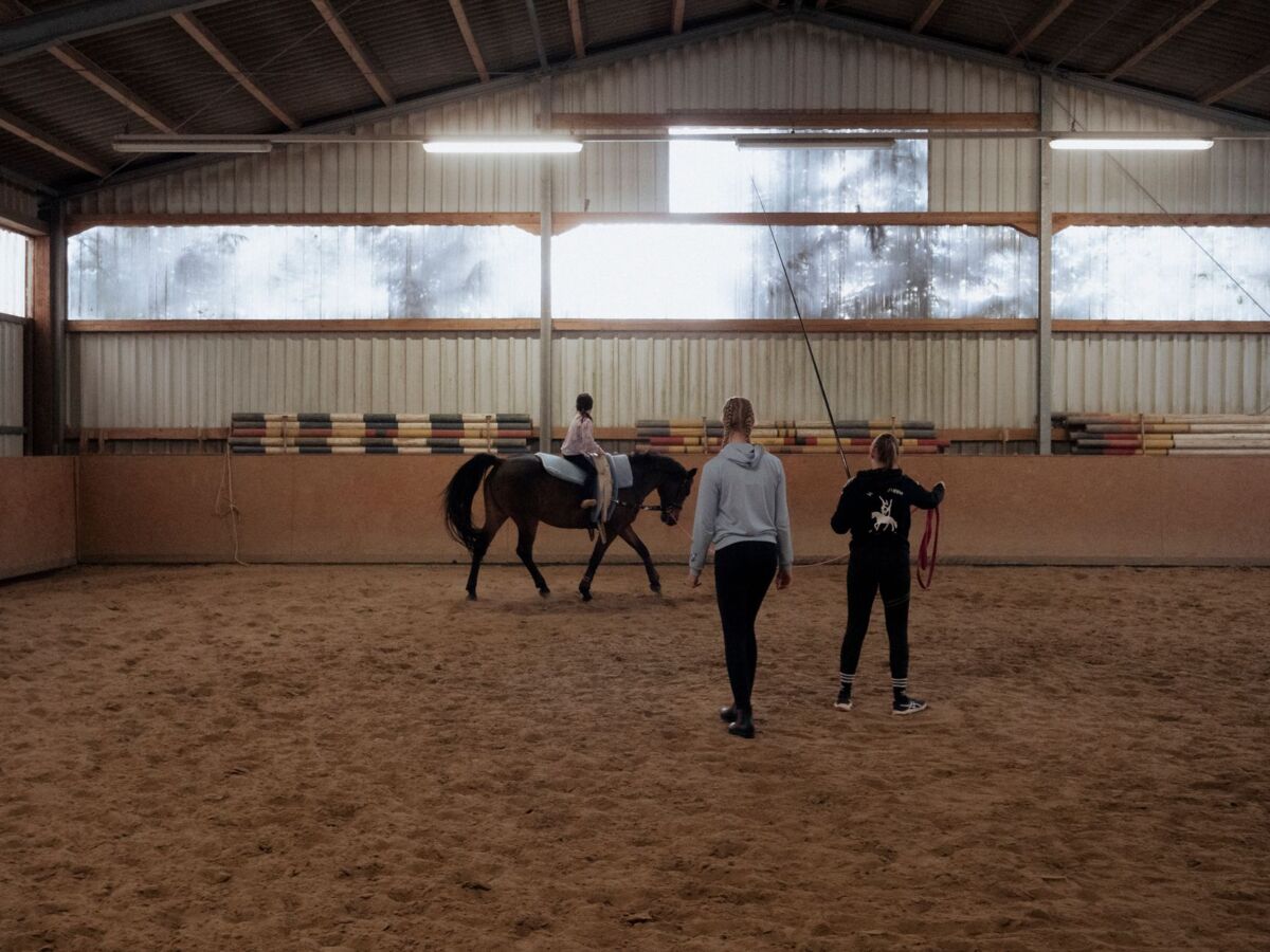 A young girl receives horse riding lessons indoors under guidance.