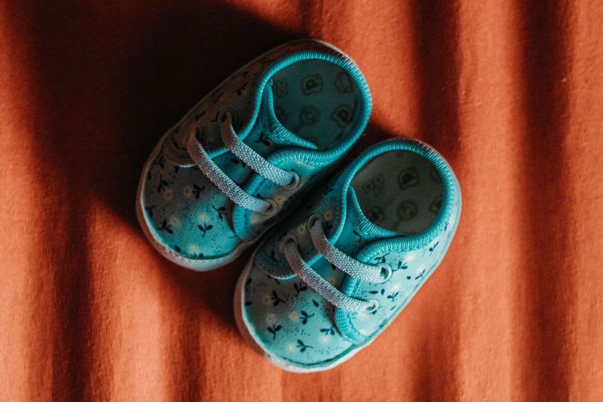 Close-up of cute blue baby shoes with floral pattern on textured orange fabric.
