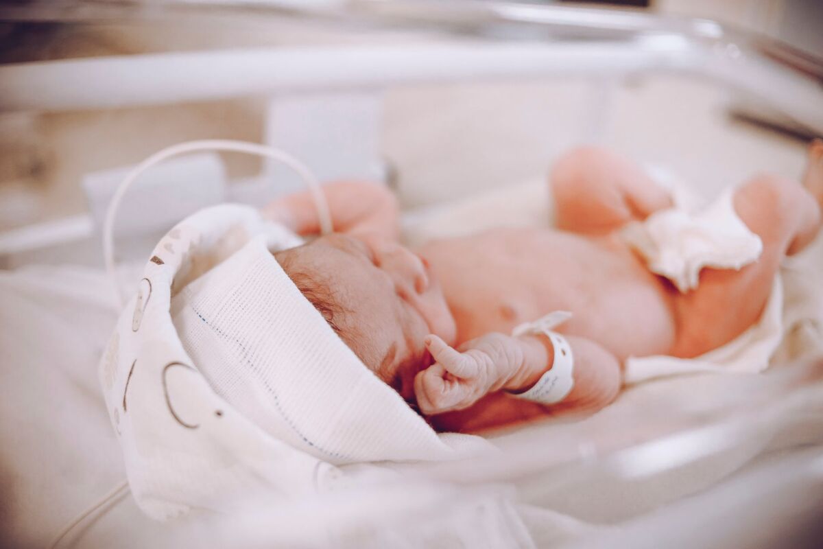 A tiny newborn baby resting peacefully in a hospital crib, swaddled in a blanket.