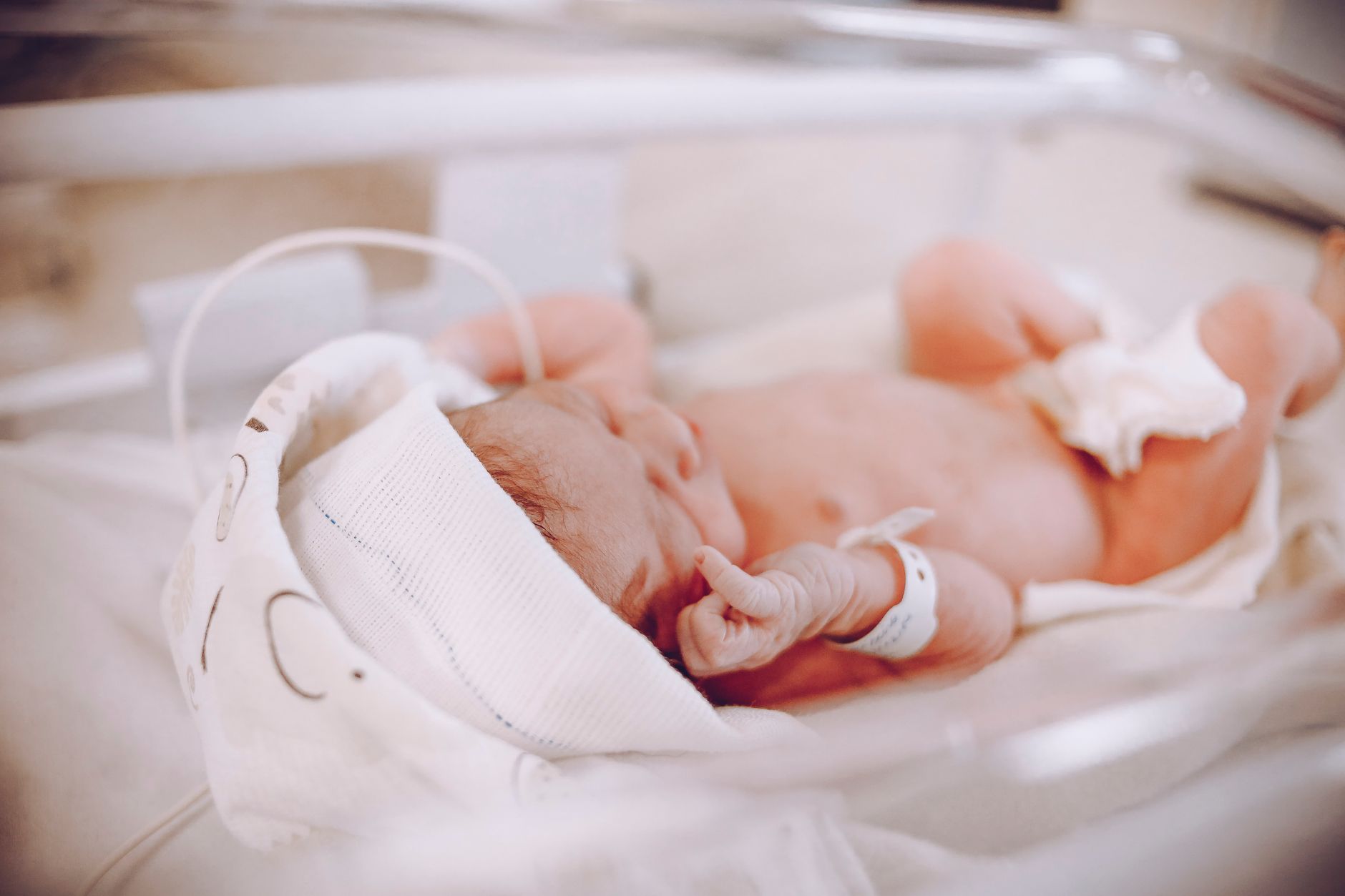 A tiny newborn baby resting peacefully in a hospital crib, swaddled in a blanket.