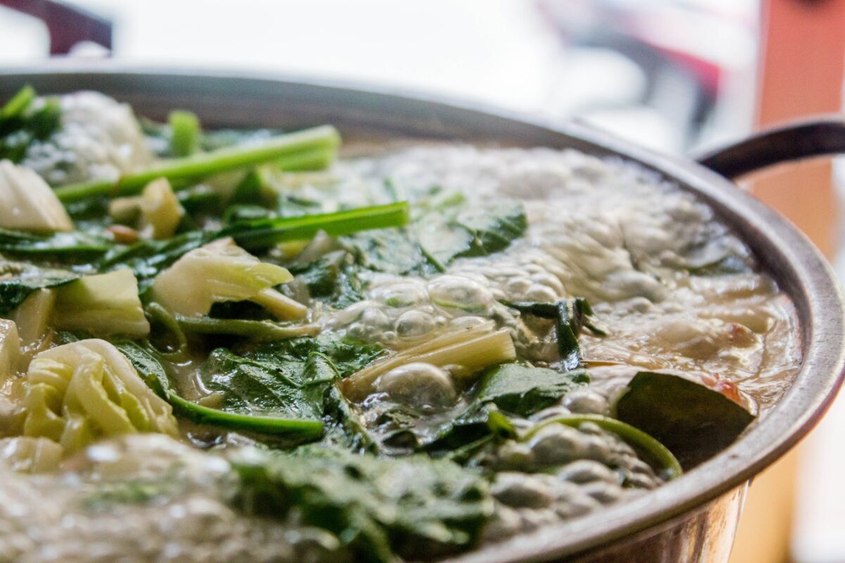 Close-up of a bubbling hot pot filled with fresh leafy greens, perfect for a flavorful meal.