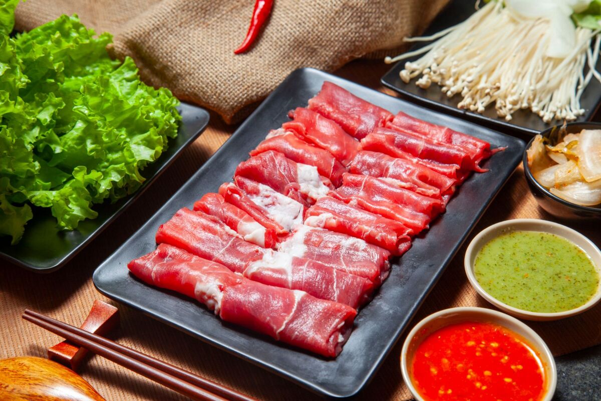 Fresh ingredients for hot pot include thinly sliced beef, lettuce, mushrooms, and dipping sauces.