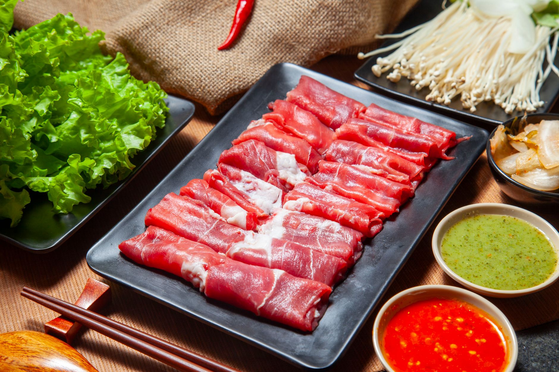 Fresh ingredients for hot pot include thinly sliced beef, lettuce, mushrooms, and dipping sauces.