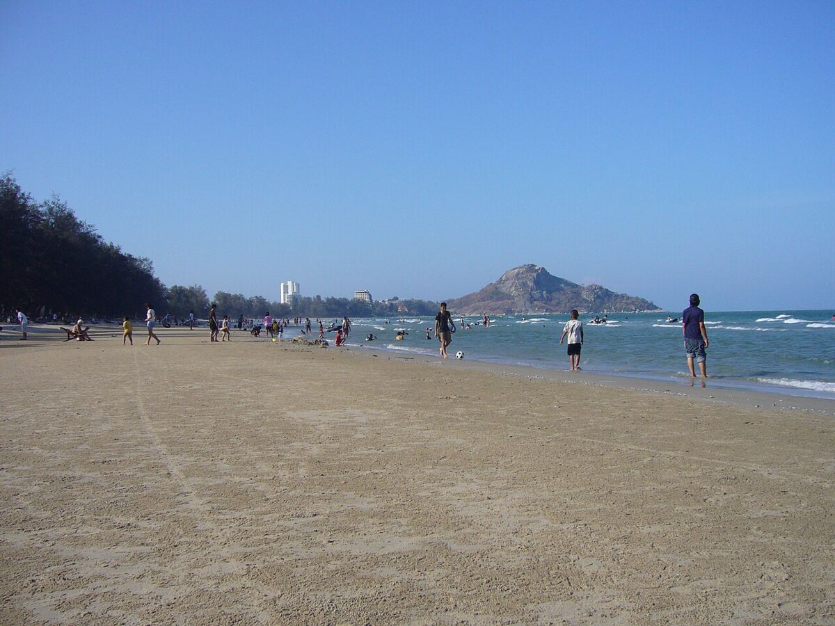 Sunset over Hua Hin Beach with people walking on the wet sand and the resort skyline glowing pink