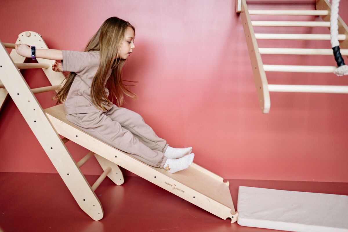 Young girl having fun on a wooden slide in an indoor playground setup.