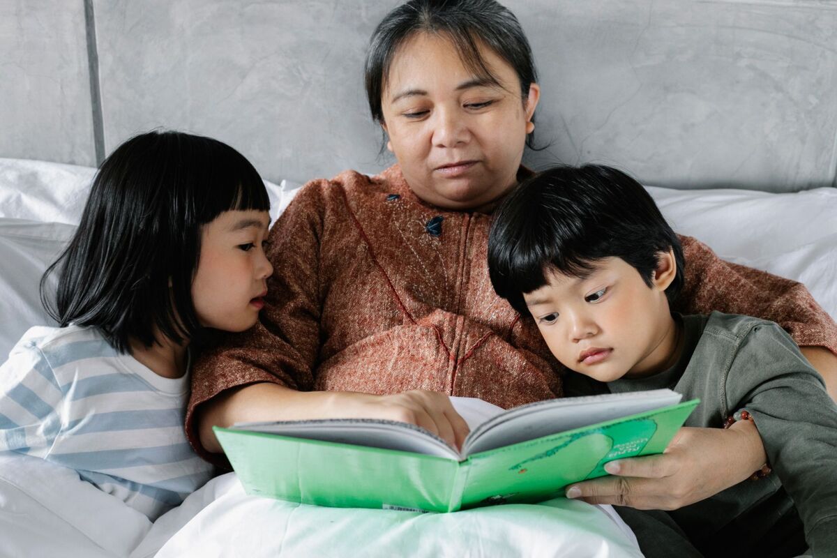 Elderly woman lying in bed and reading book for kids while spending weekend at home