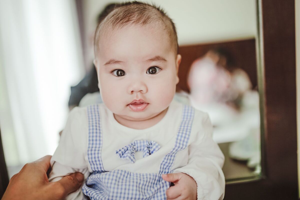 Adorable little Asian baby wearing white and blue cotton bodysuit sitting and looking at camera