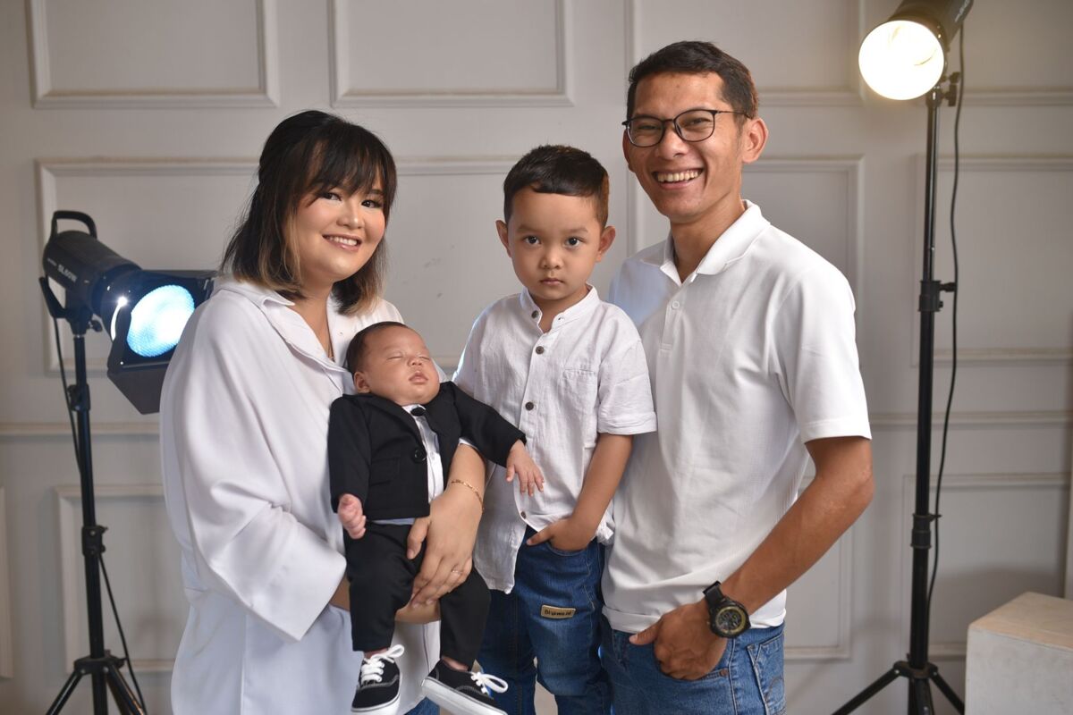 A joyful family portrait featuring parents with their newborn and older child in a studio setting.