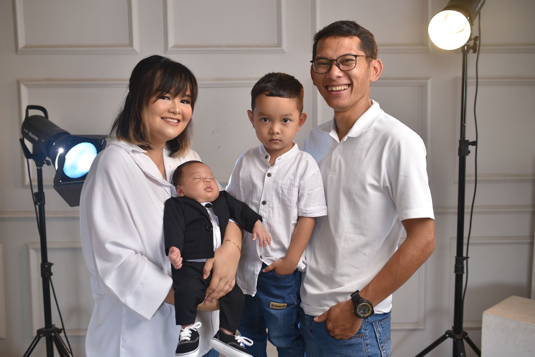A joyful family portrait featuring parents with their newborn and older child in a studio setting.
