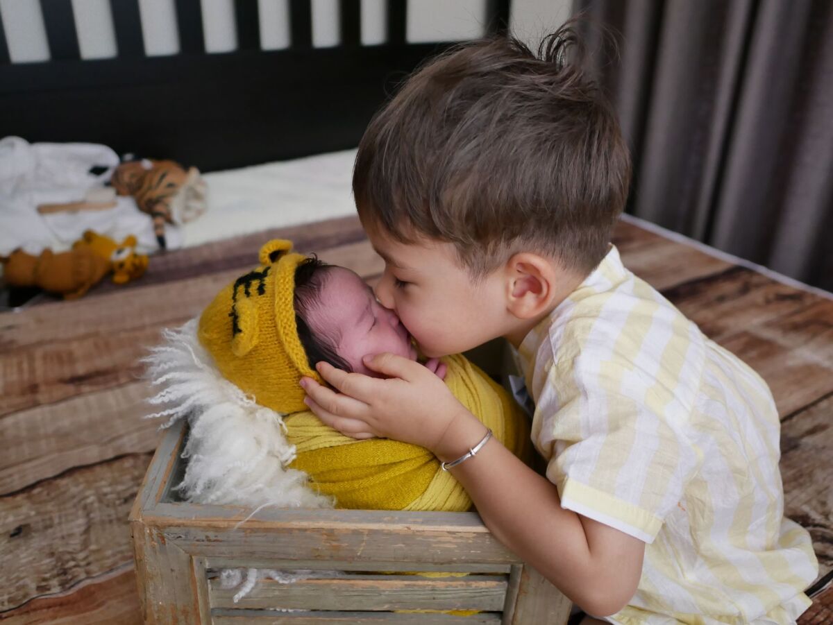 A touching moment of sibling love as a boy kisses his baby sibling wrapped in yellow in a wooden crate.