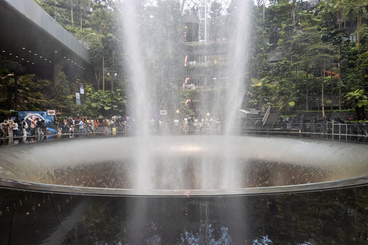 Ground-level view of the Rain Vortex waterfall splashing into its circular basin with visitors watching around the Forest Valley at Jewel Changi Airport