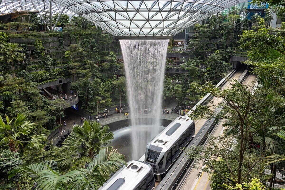A Changi Airport Skytrain gliding past the Rain Vortex waterfall and surrounding indoor rainforest at Jewel Changi Airport