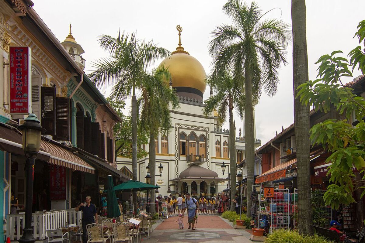 The golden dome of Sultan Mosque framed by palm trees at the end of a pedestrian street lined with cafes in Kampong Glam, Singapore
