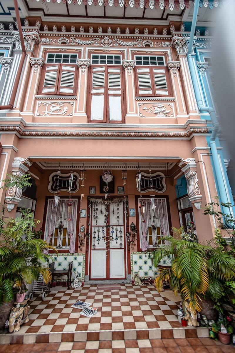 Detailed facade of a pink Peranakan shophouse in Joo Chiat with carved plaster trim, louvred windows and a tiled entrance