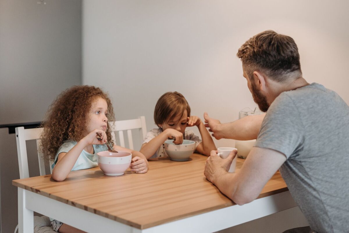 A father and his children having breakfast together at a wooden table indoors, promoting family bonding.