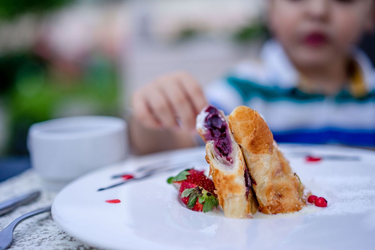 A child reaches for a delicious fruit-filled pastry dessert on a white plate with strawberries.