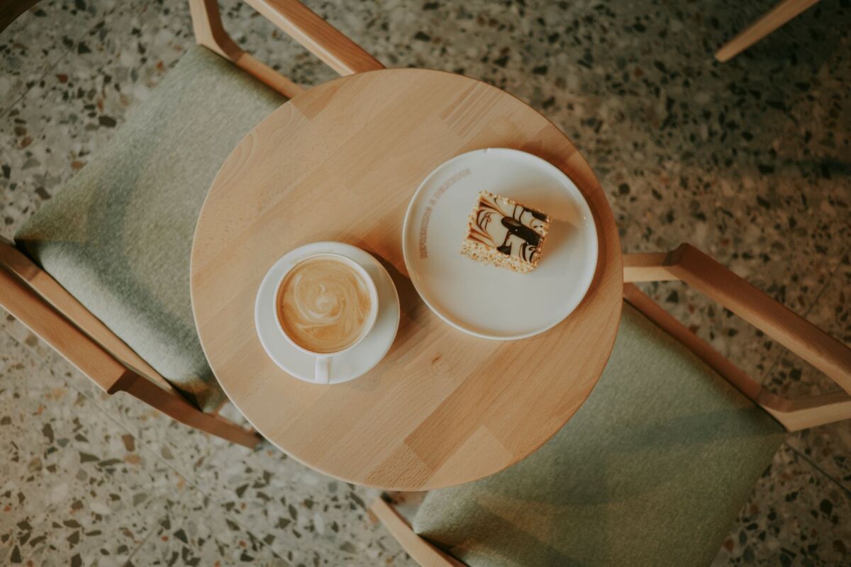 Top view of a coffee cup and dessert slice on a cafe table with chairs.