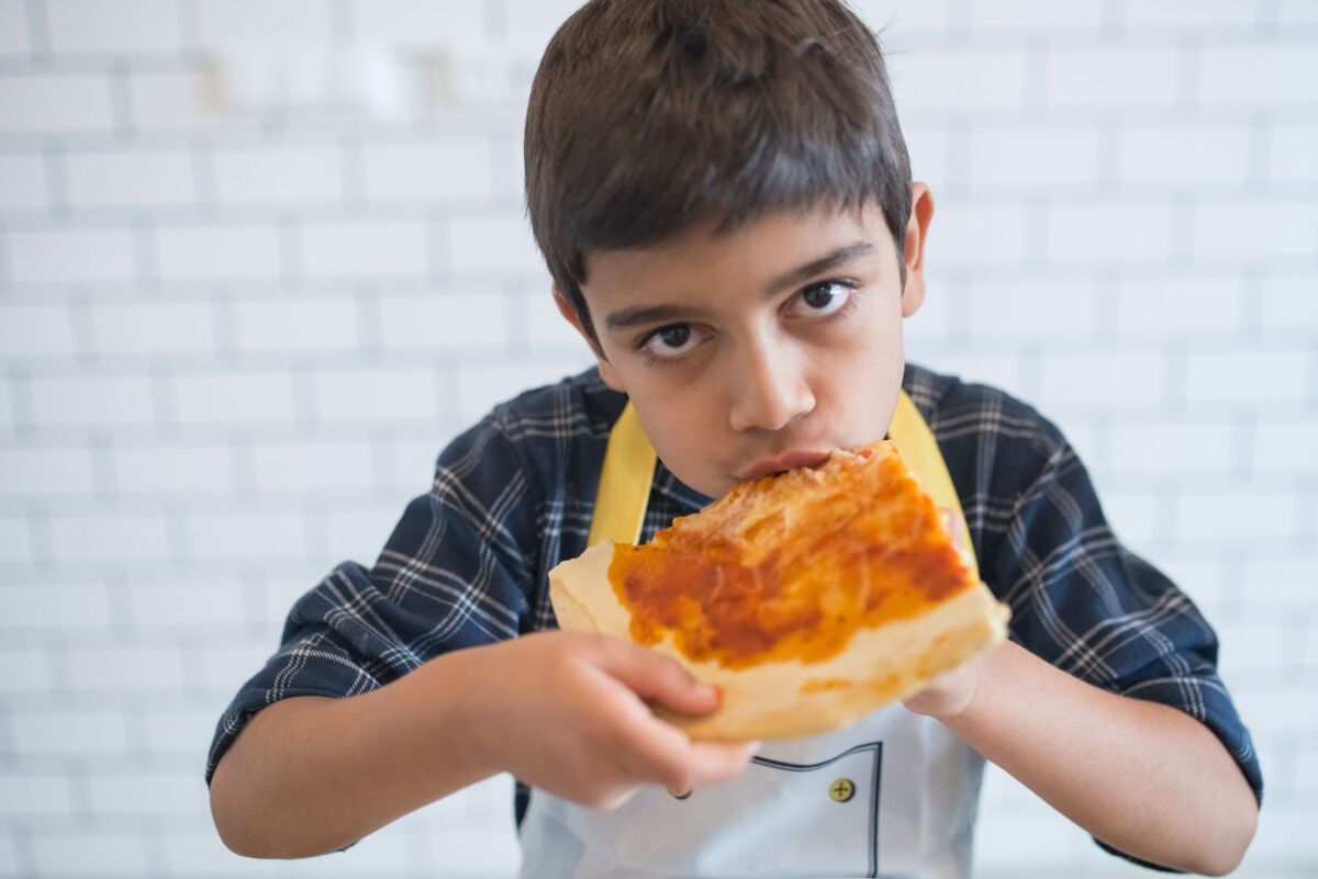 A young boy in a plaid shirt enjoys a slice of pizza indoors, showcasing casual dining.