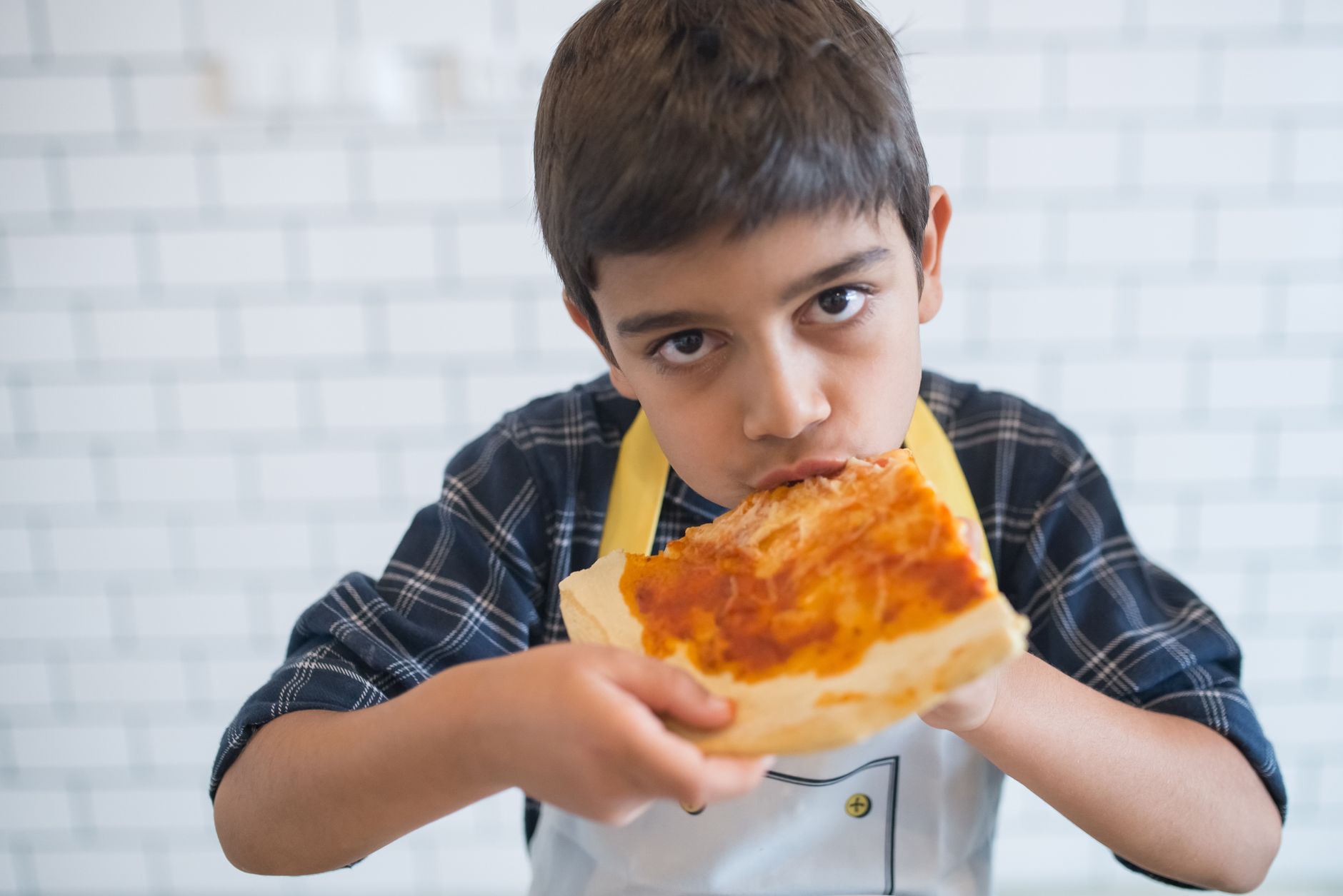 A young boy in a plaid shirt enjoys a slice of pizza indoors, showcasing casual dining.