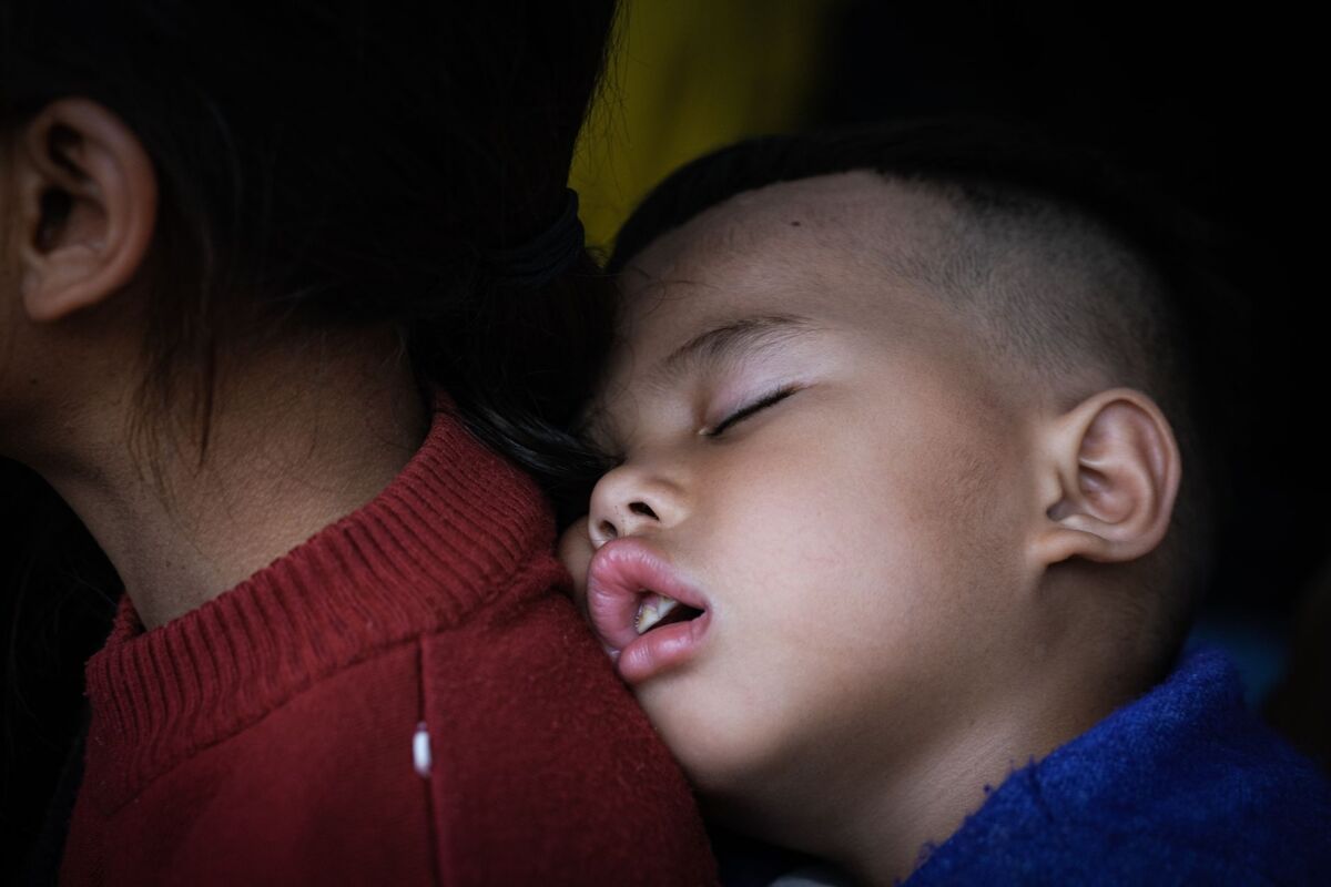 A young child sleeping peacefully while resting against his mother's back, conveying warmth and security.