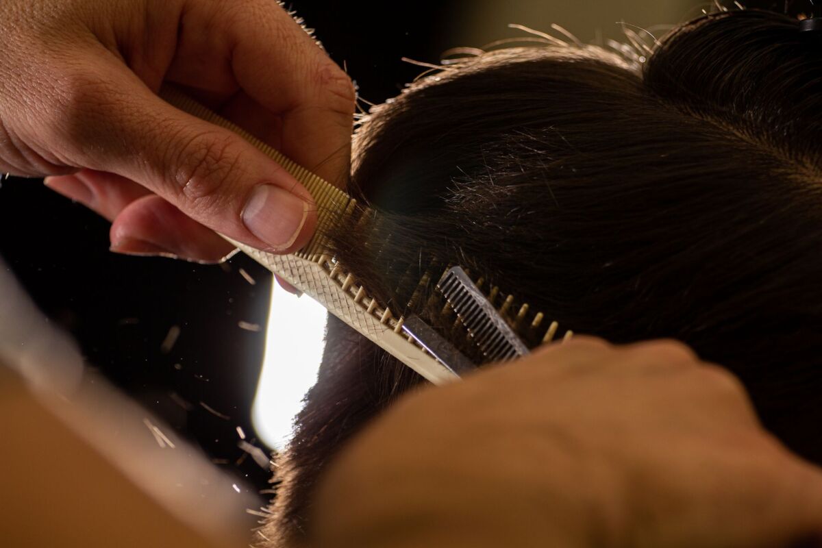 Close-up of a stylist trimming hair with a comb and scissors indoors.