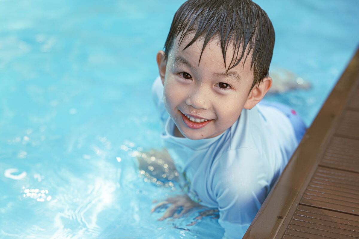 Happy Asian boy swimming and having fun in a pool on a sunny day in Jakarta, Indonesia.