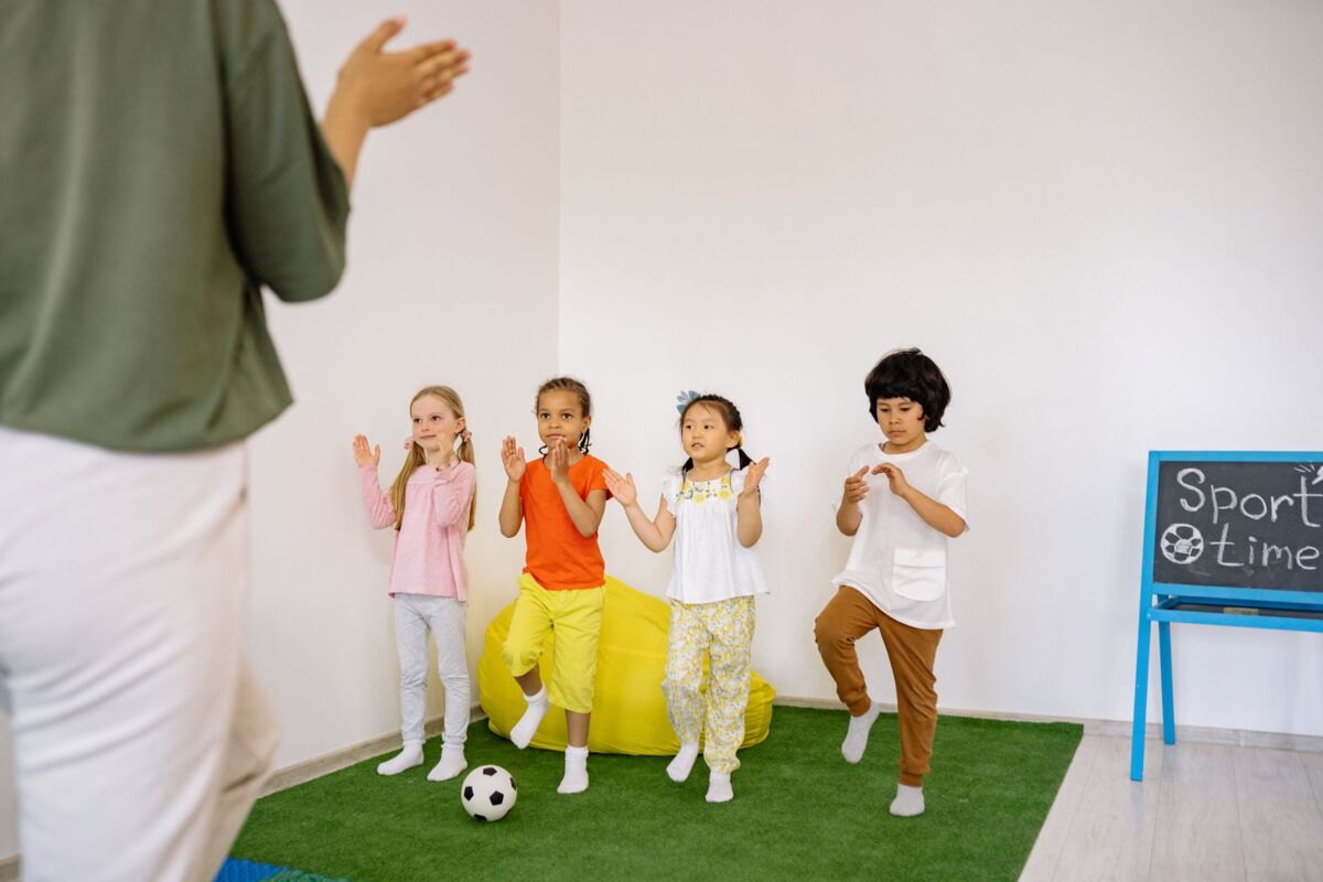 A group of preschool children participating in a fun indoor sports activity led by a teacher.