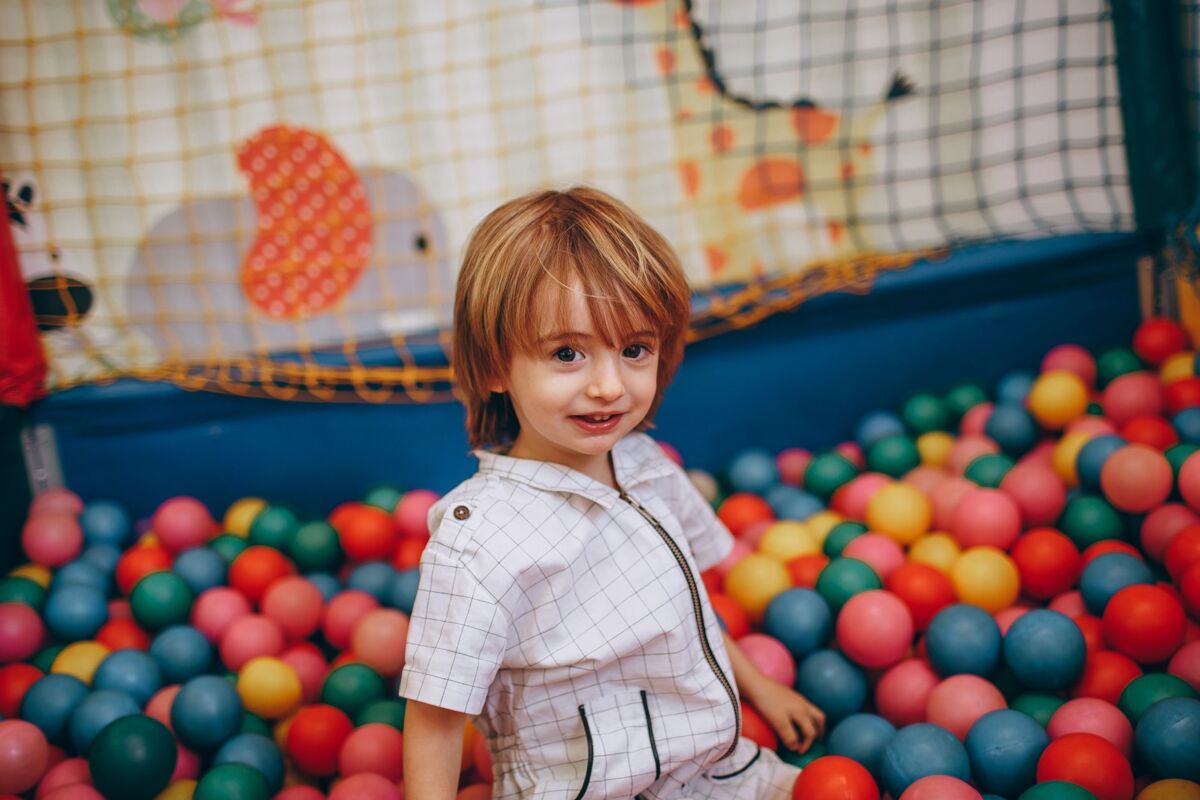 A young child enjoys playing in a colorful ball pit indoors, showcasing joy and creativity.