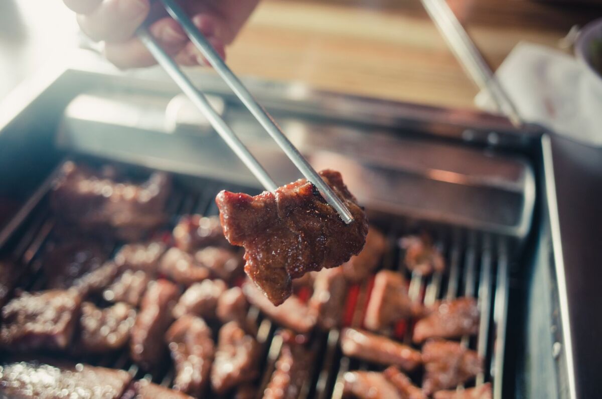 Juicy meat being grilled on a barbecue, captured close-up with chopsticks.