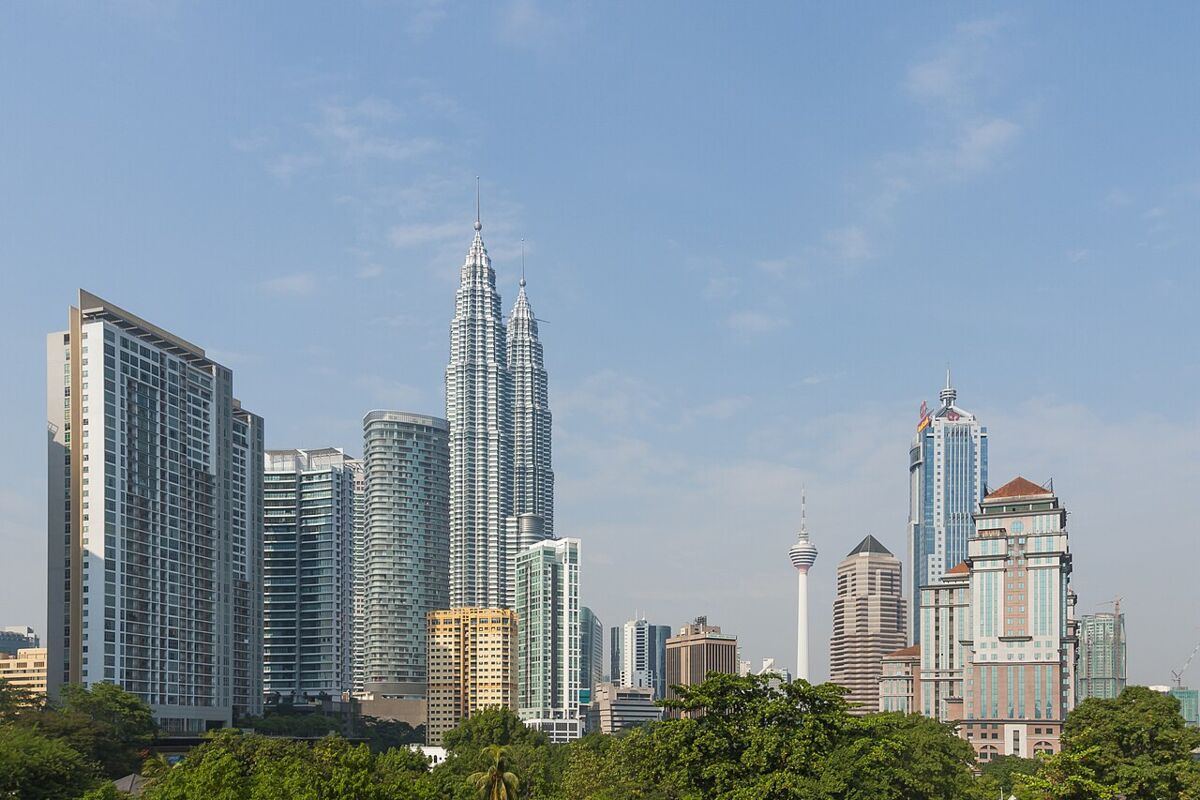 Daytime Kuala Lumpur skyline with the Petronas Towers and KL Tower above green parkland