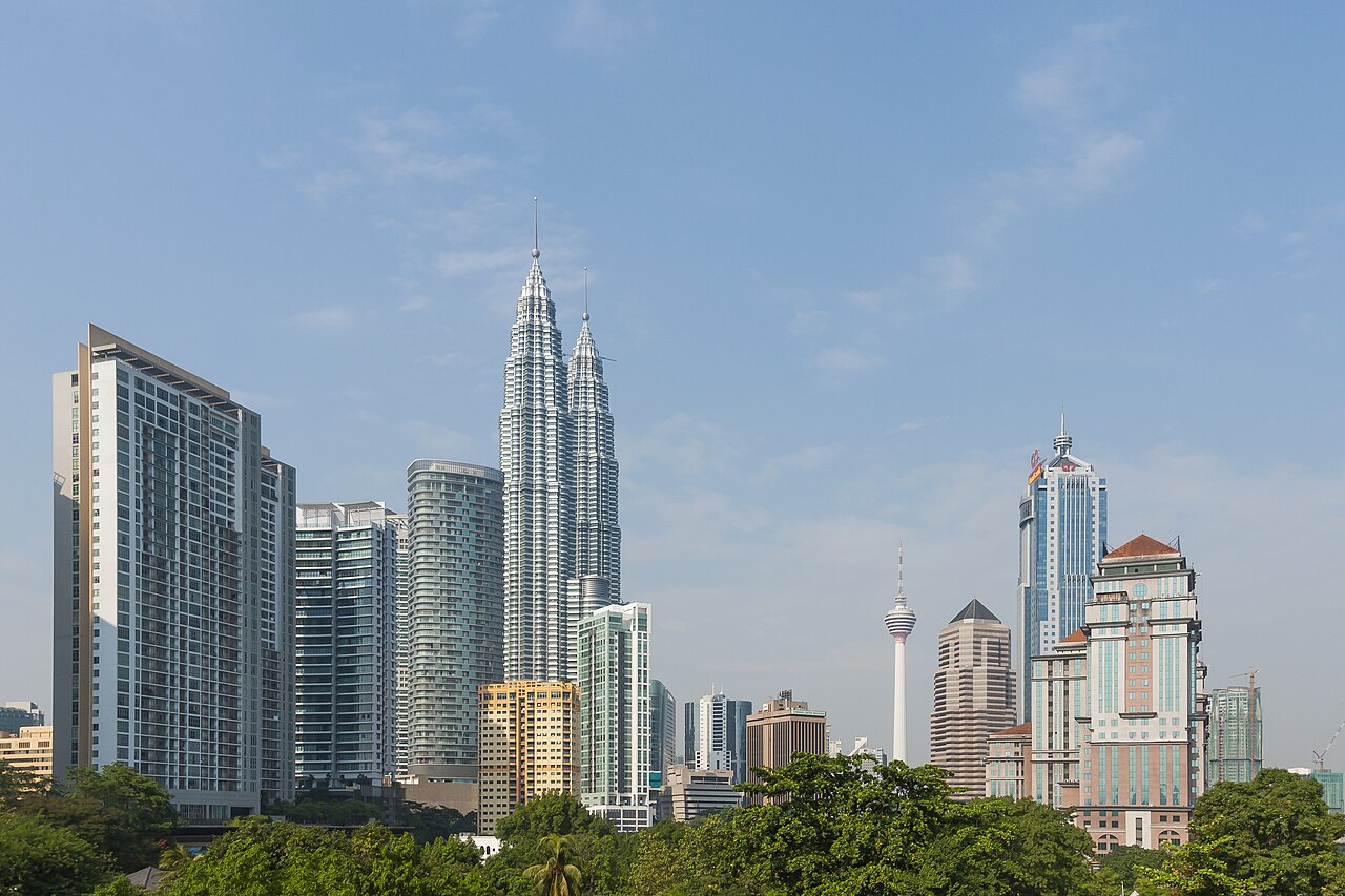 Daytime Kuala Lumpur skyline with the Petronas Towers and KL Tower above green parkland