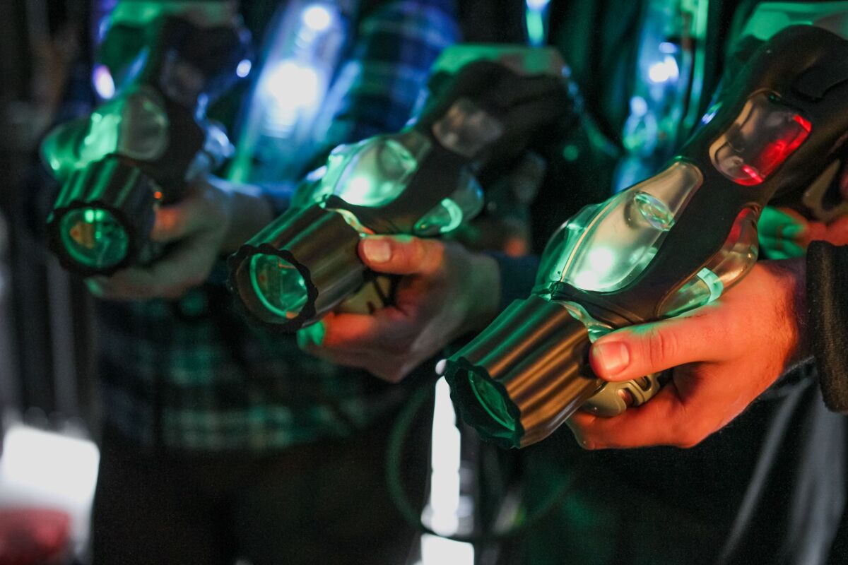 Close-up of players holding illuminated laser tag guns indoors.