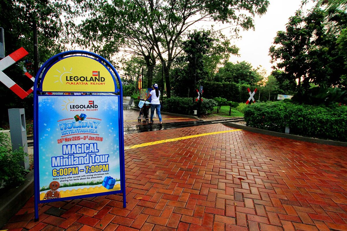 Legoland Malaysia Resort entrance signboard advertising a Miniland tour, with a parent pushing a stroller along a brick path