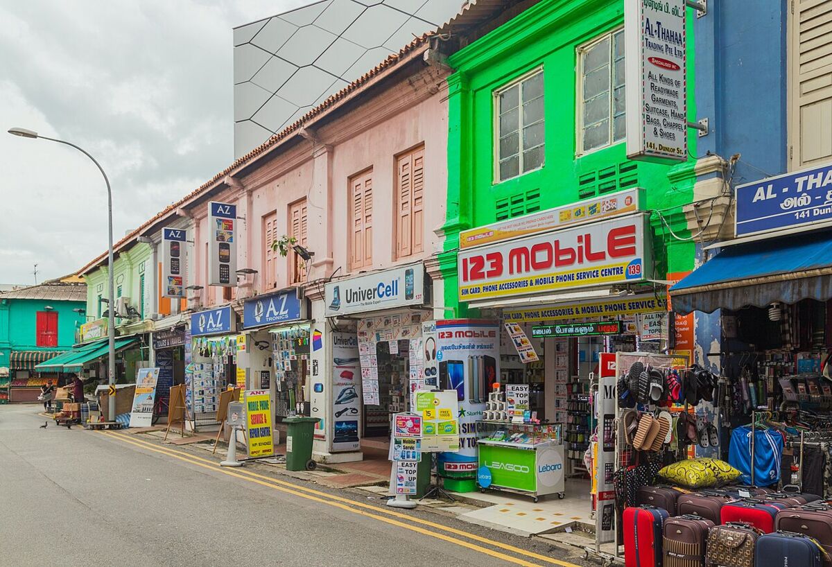 Busy row of shops along Dunlop Street in Little India, with a bright green shopfront and colourful signage and goods spilling onto the pavement