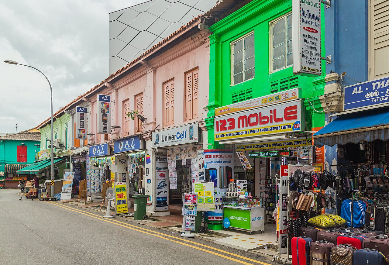Busy row of shops along Dunlop Street in Little India, with a bright green shopfront and colourful signage and goods spilling onto the pavement