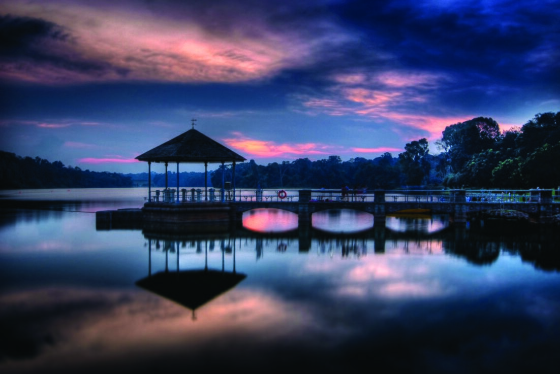 The pavilion and arched bridge at Lower Peirce Reservoir reflected in calm water at dusk