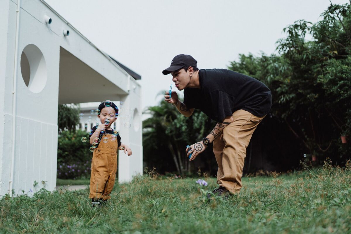 Asian father and son enjoying a playful moment blowing bubbles in the backyard.