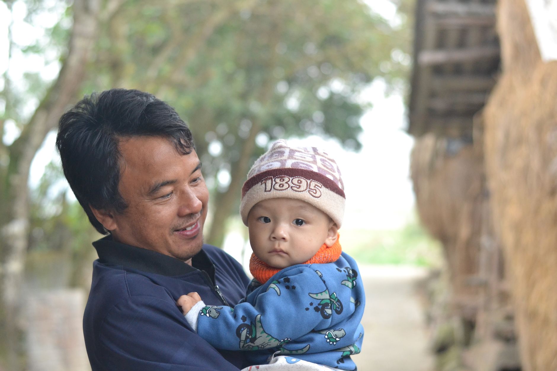 Asian father joyfully holding his baby son outdoors. Happy family moment captured.