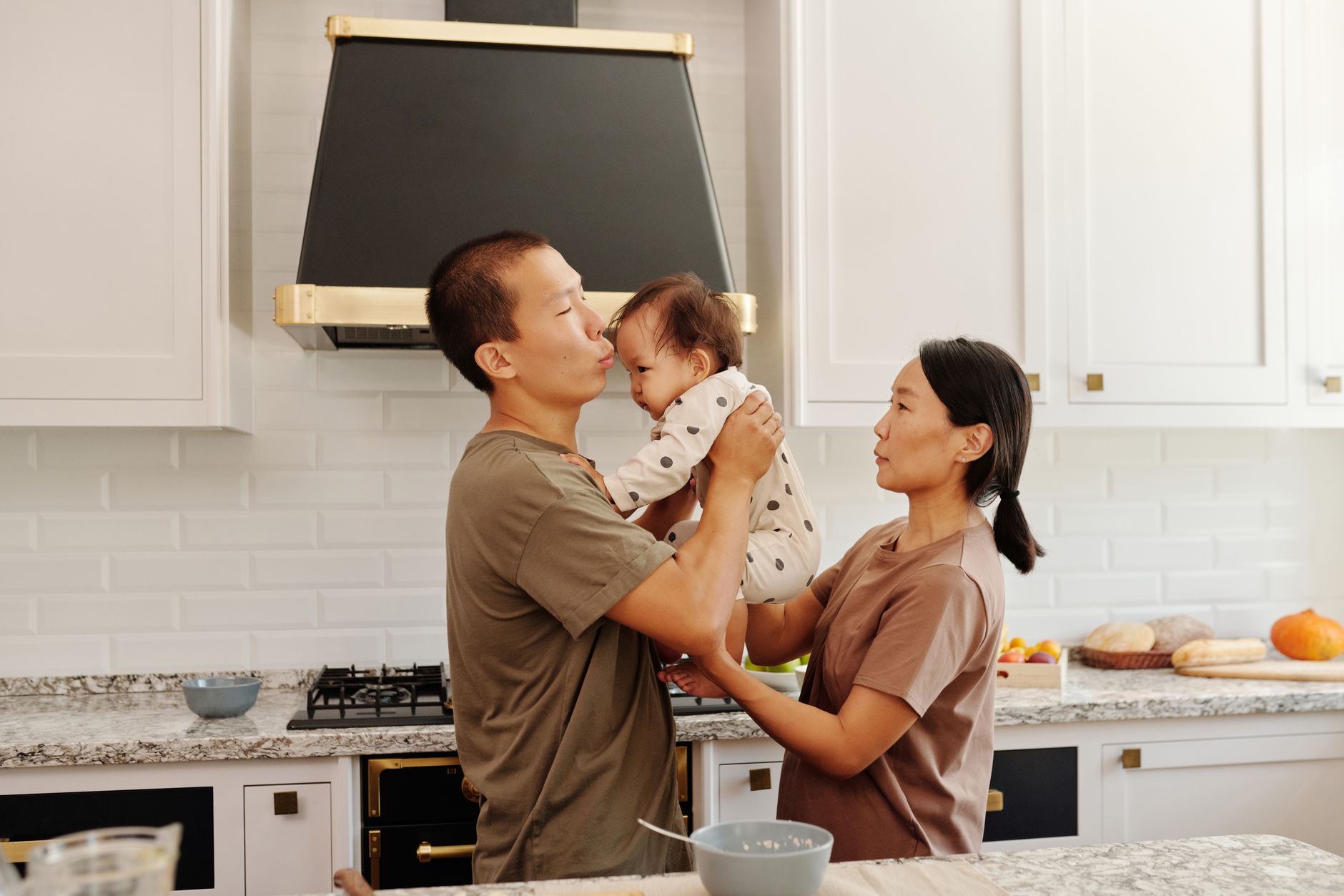 Asian family enjoying bonding time in their modern kitchen. Parents holding baby with joy.