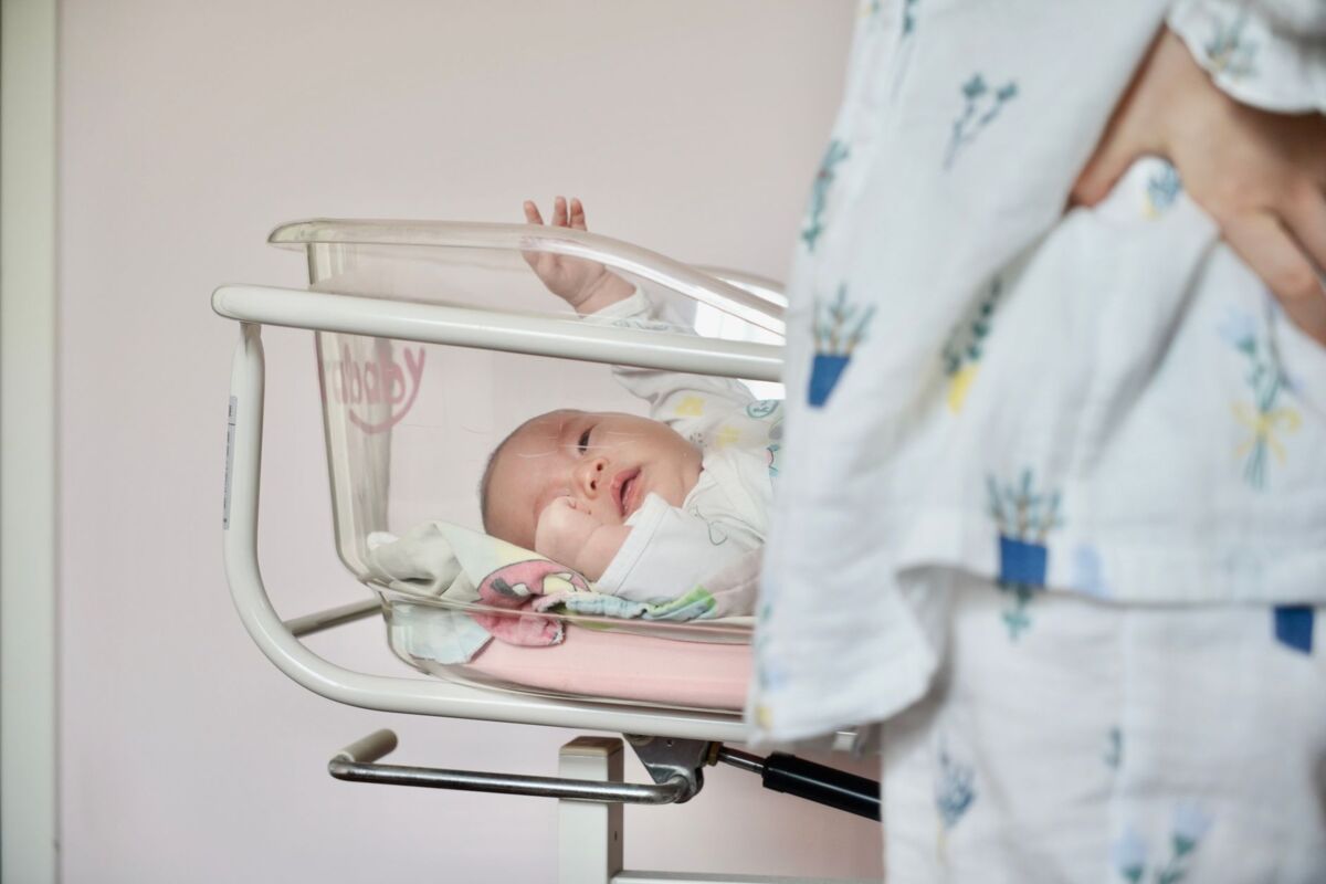 A tender scene of a newborn baby lying in a hospital bassinet with the mother standing close by.